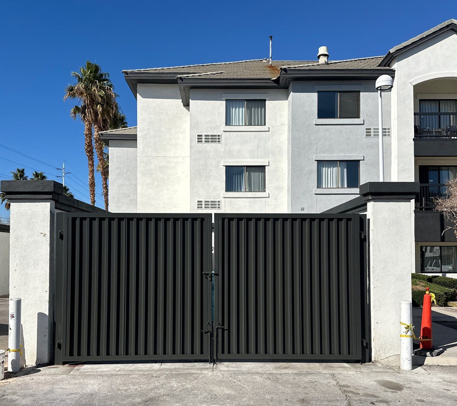 Curved black metal railing around a small yard by a beige house, with gravel and a propane tank.