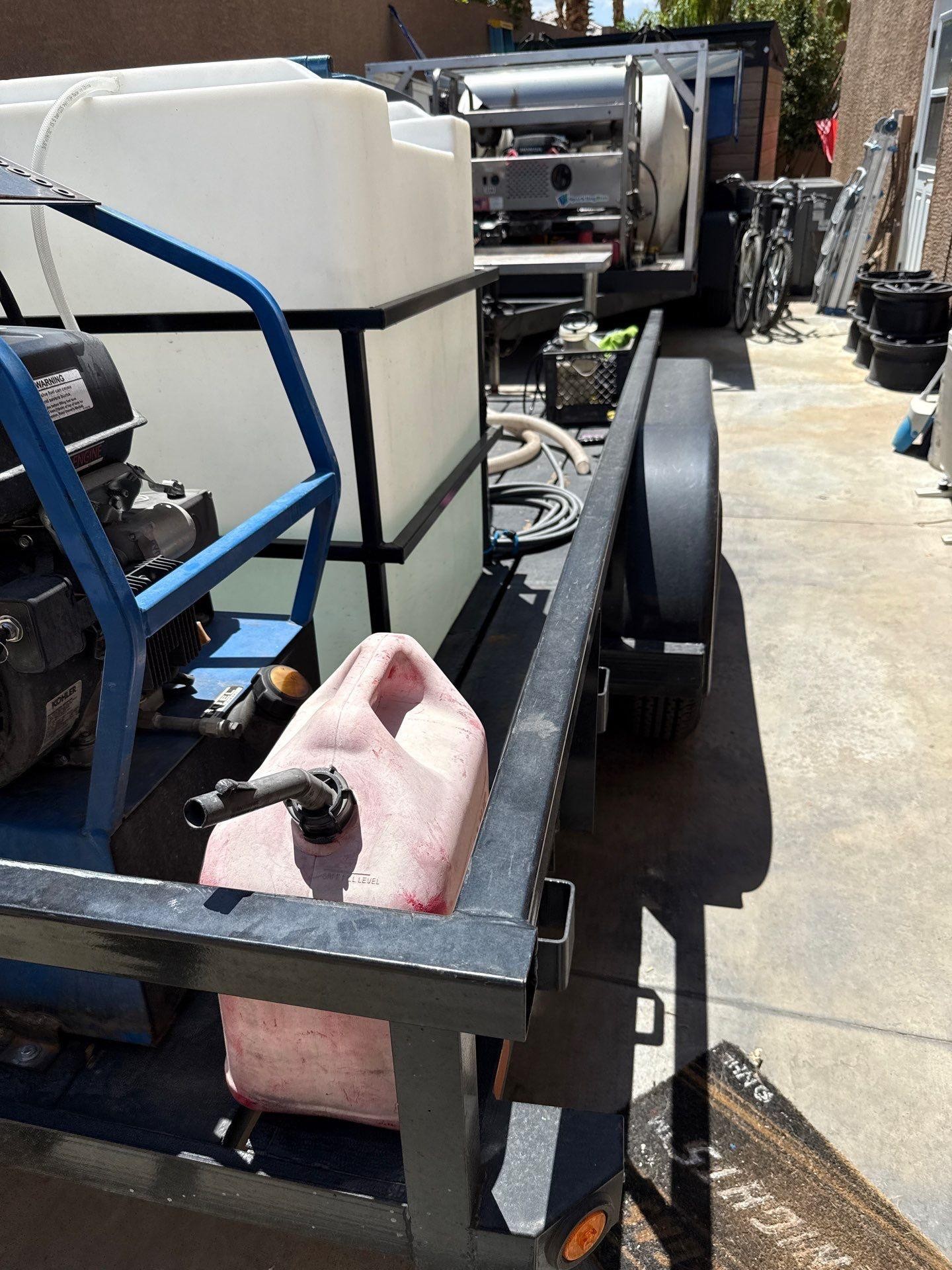 Trailer frame carrying a large white plastic tank and a pink jerry can on a concrete surface.