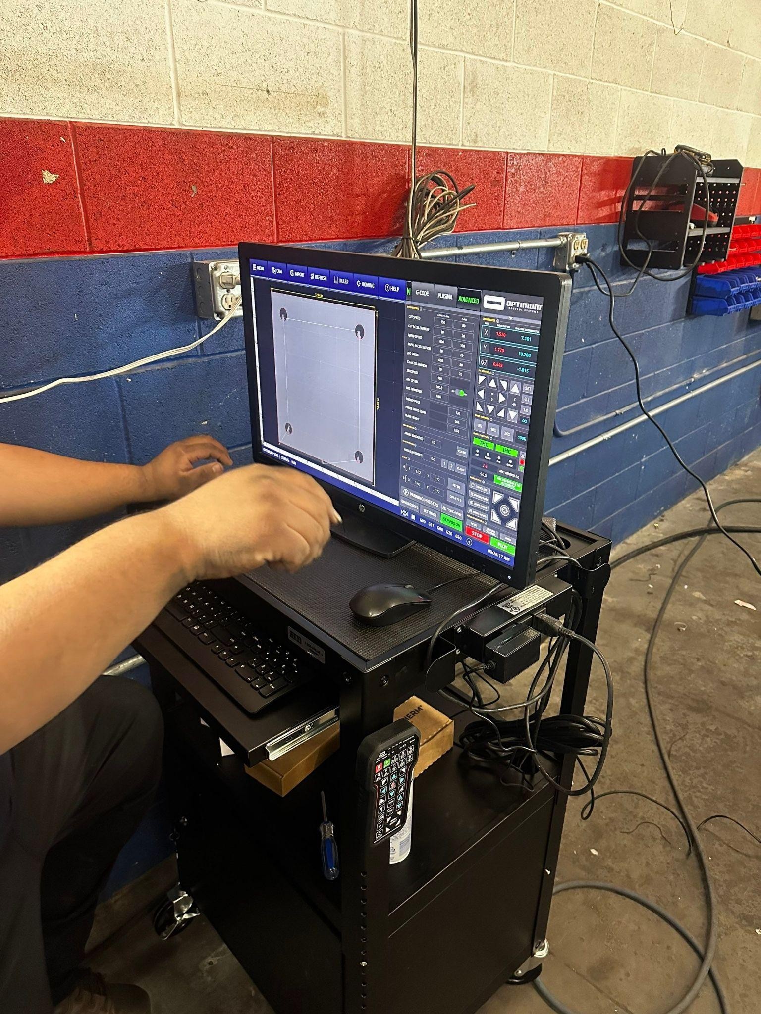 Workshop scene: operator at a laptop controlling a large cutting machine; screen shows machining software.