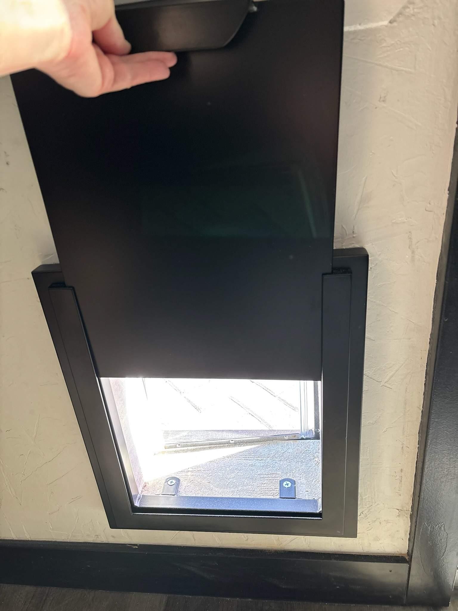 Wall opening with a dark frame and lower glass panel; a hand near the top edge.