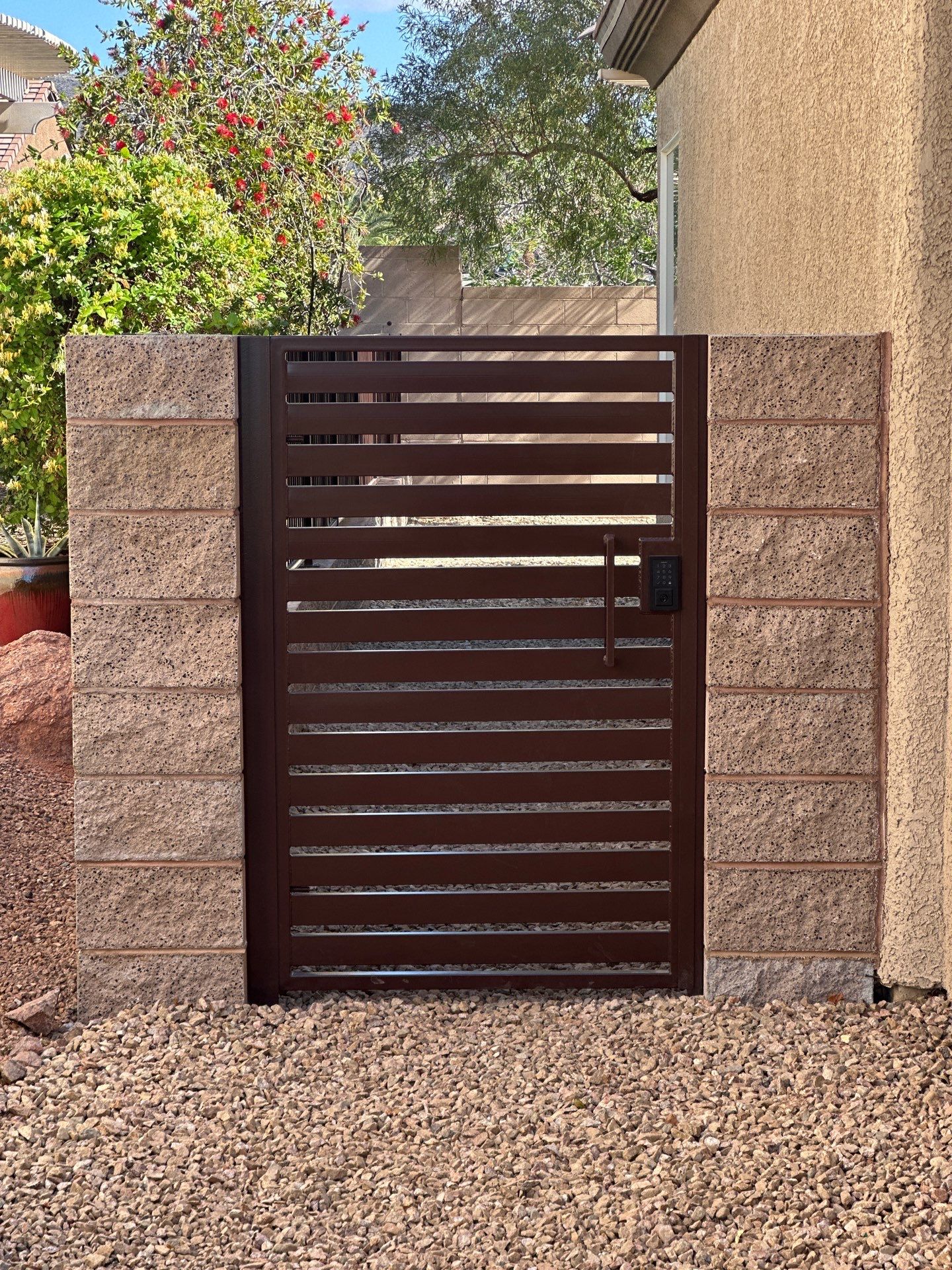 Brown horizontal slat gate between brick columns on a gravel path.