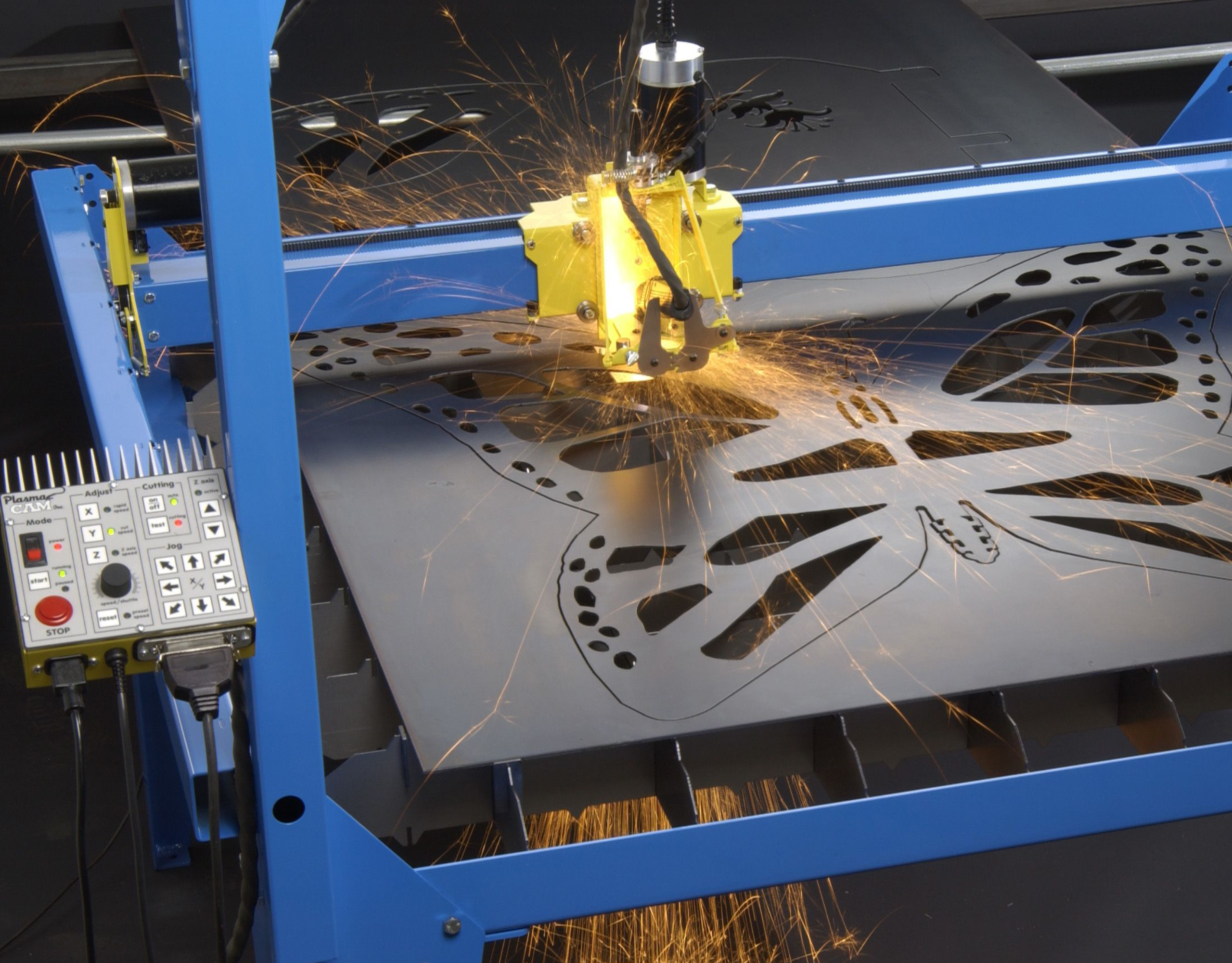 Industrial laser cutter cutting decorative metal sheet with flower-shaped cutouts; sparks fly from the cutting head.